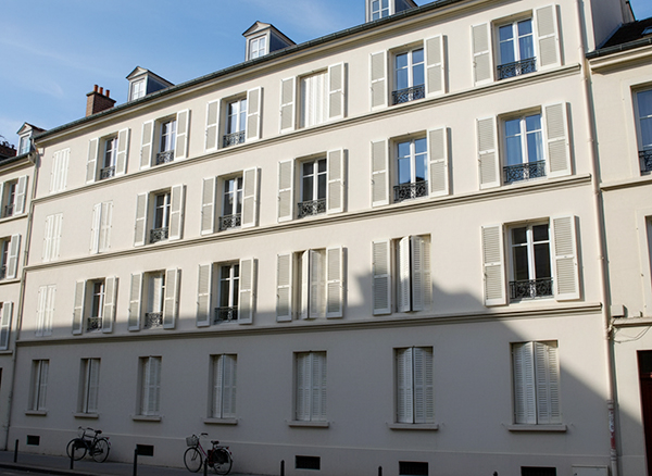 Façade d'immeuble parisien avec persiennes métalliques dans une rue étroite soumise à l'effet canyon urbain